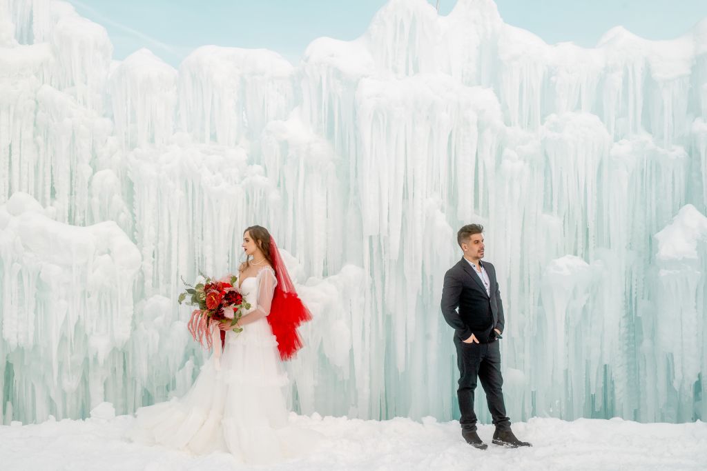 Utah Bridals at Ice Castles in Midway with Wed Utah's maximalist bouquet and bright red bridal drop veil. Andrea (groom model) and Kalli (bride model) stand opposite of each other facing opposite directions.