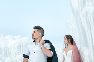 Andrea LaFra & Kalli Hofhines pose at the ice castles in a modern bridal pose featuring the groom up front with his suit coat over his shoulder.
